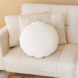 Cream boucle round cushion with a soft, textured surface and a golden metallic trim on the edge, placed on a modern beige sofa.