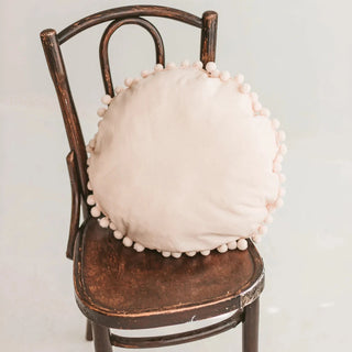 Beige cushion with pompom trim styled on a chair