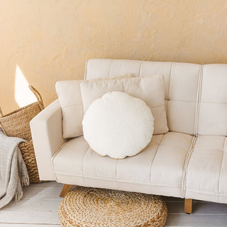 Elegant round cushion in cream boucle with a shimmering gold trim, styled on a bed with neutral linens.