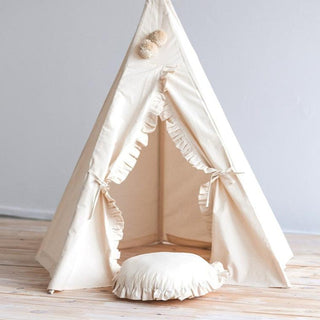 A beige round cushion with ruffled trim styled next to a matching ruffled teepee in a cozy kids' room.